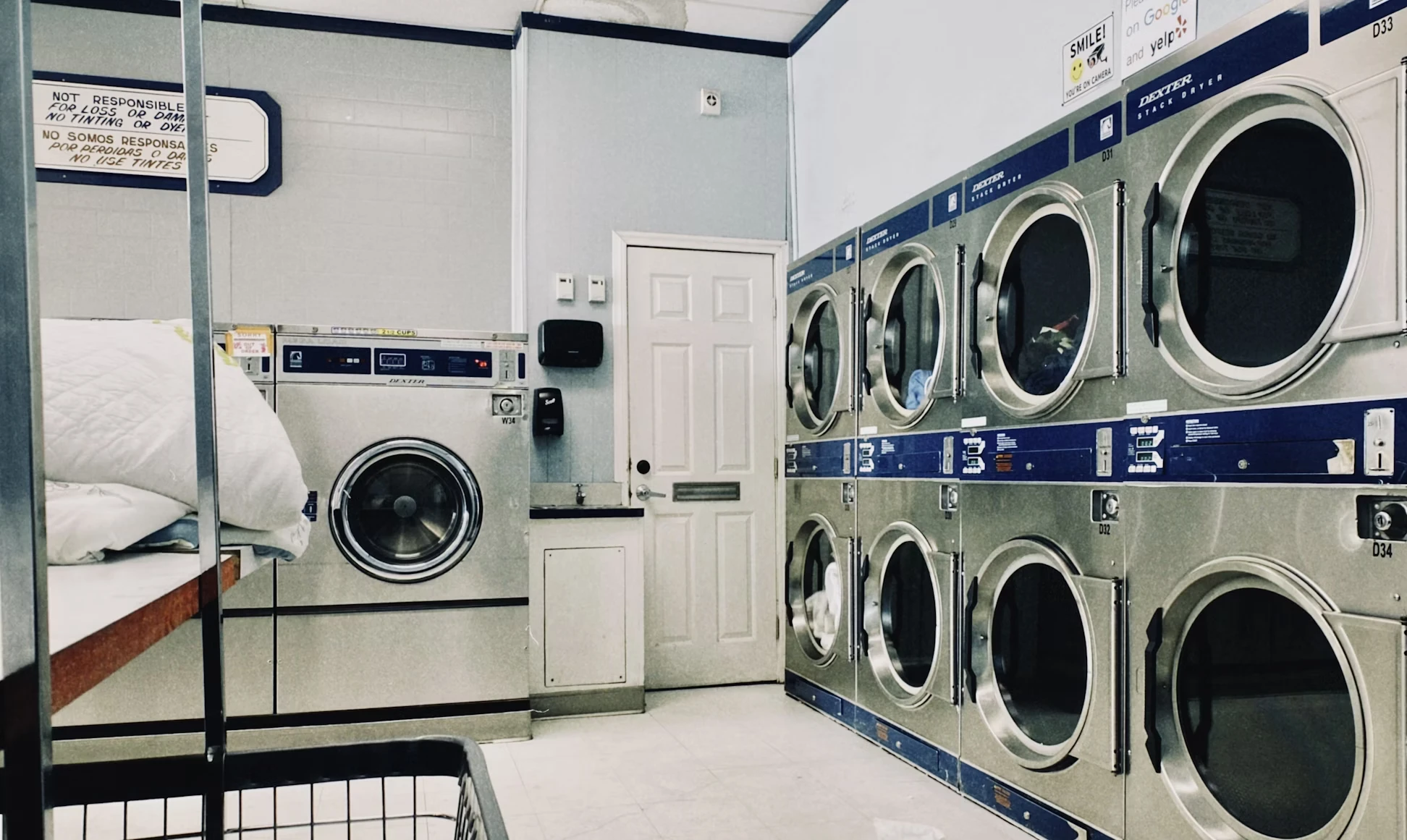 Interior of a laundromat with stacked Dexter brand dryers on the right and a washing machine on the left next to a white door.